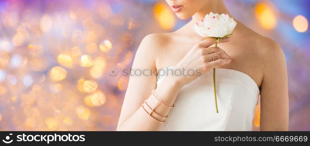 beauty, jewelry and luxury concept - close up of beautiful woman with golden ring and bracelet holding flower over holidays lights background. close up of beautiful woman with ring and bracelet. close up of beautiful woman with ring and bracelet