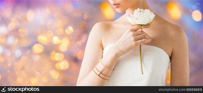 beauty, jewelry and luxury concept - close up of beautiful woman with golden ring and bracelet holding flower over holidays lights background. close up of beautiful woman with ring and bracelet. close up of beautiful woman with ring and bracelet