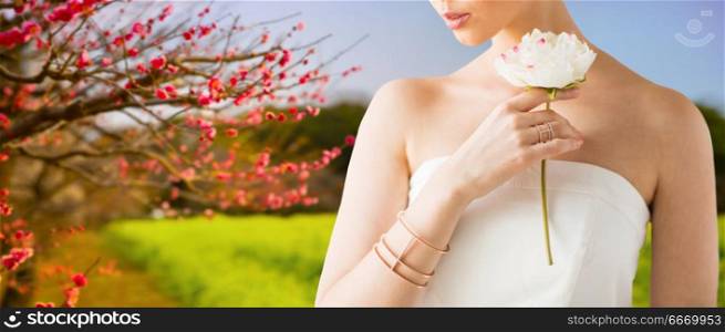 beauty, jewelry and luxury concept - close up of beautiful woman with golden ring and bracelet holding flower over natural spring cherry blossom background. close up of beautiful woman with ring and bracelet. close up of beautiful woman with ring and bracelet