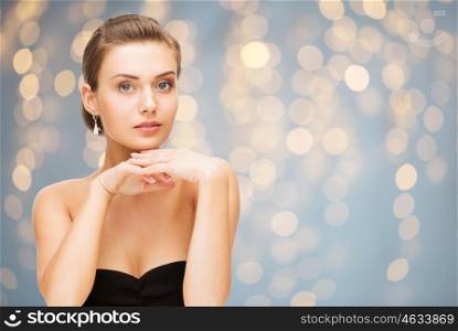 beauty, jewelry, holidays and people concept - beautiful woman in evening dress wearing diamond earrings over lights background