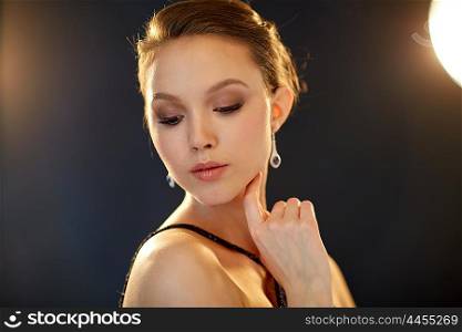 beauty, jewelry, night life, people and luxury concept - beautiful asian woman with diamond earring over black background and spotlights