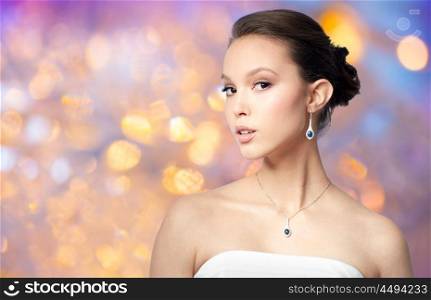 beauty, jewelry, people and luxury concept - beautiful asian woman or bride with earring and pendant over holidays lights background. beautiful asian woman with earring and pendant. beautiful asian woman with earring and pendant