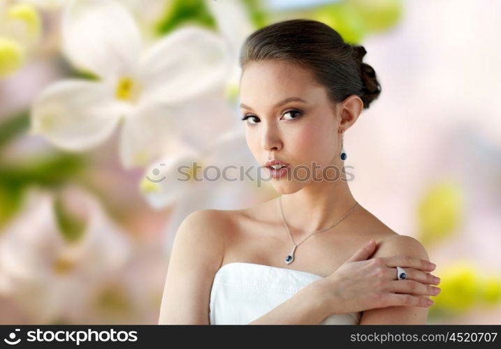 beauty, jewelry, people and luxury concept - beautiful asian woman or bride with earring, finger ring and pendant over natural spring lilac blossom background