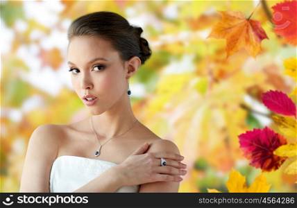 beauty, jewelry, people and luxury concept - beautiful asian woman or bride with earring, finger ring and pendant over autumn leaves background