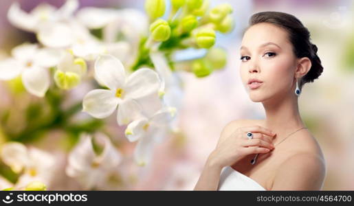 beauty, jewelry, people and luxury concept - beautiful asian woman or bride with earring, finger ring and pendant over natural spring lilac blossom background