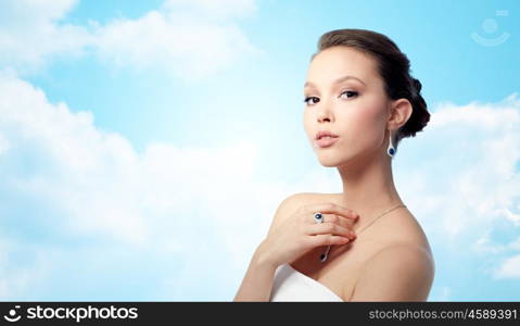 beauty, jewelry, people and luxury concept - beautiful asian woman or bride with earring, finger ring and pendant over blue sky and clouds background