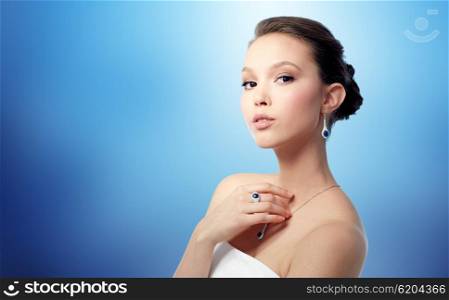 beauty, jewelry, people and luxury concept - beautiful asian woman or bride with earring, finger ring and pendant over blue background
