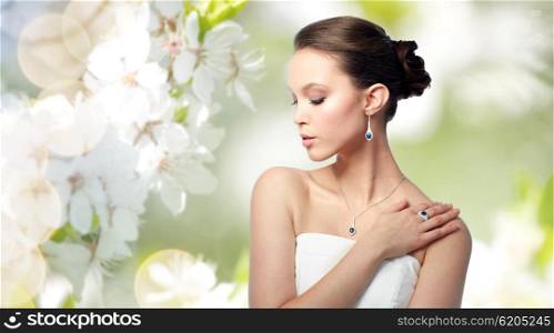 beauty, jewelry, people and luxury concept - beautiful asian woman or bride with earring, finger ring and pendant over natural spring cherry blossom background