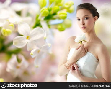 beauty, jewelry, people and luxury concept - beautiful asian woman or bride in white dress with peony flower, golden ring and bracelet over natural spring lilac blossom background
