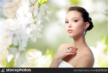 beauty, jewelry, people and luxury concept - beautiful asian woman or bride with earring, finger ring and pendant over natural spring cherry blossom background