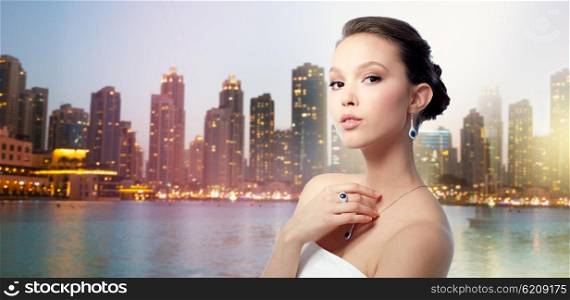 beauty, jewelry, people and luxury concept - beautiful asian woman or bride with earring, finger ring and pendant over evening dubai city lights and skyscrapers background