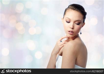 beauty, jewelry, people and luxury concept - beautiful asian woman or bride with earring and finger ring over blue holidays lights background