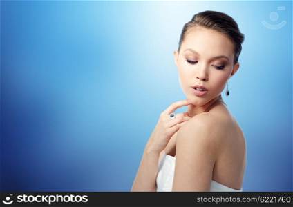 beauty, jewelry, people and luxury concept - beautiful asian woman or bride with earring and finger ring over blue background