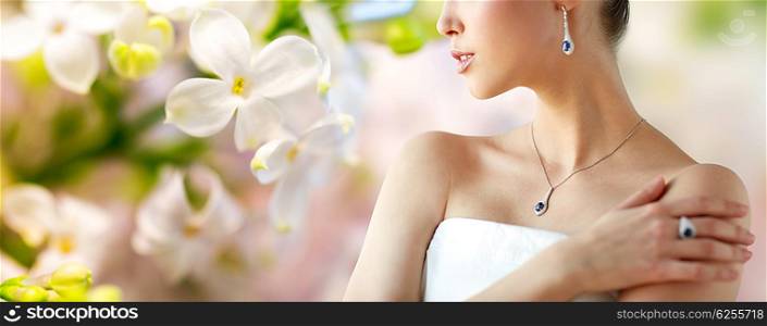 beauty, jewelry, people and luxury concept - beautiful asian woman or bride with earring, finger ring and pendant over natural spring lilac blossom background