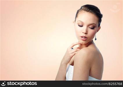 beauty, jewelry, people and luxury concept - beautiful asian woman or bride with earring and finger ring over beige background