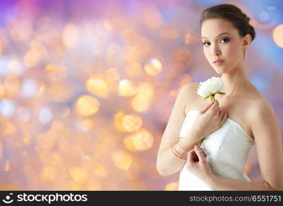 beauty, jewelry, people and luxury concept - beautiful asian woman or bride in white dress with peony flower, golden ring and bracelet over holidays lights background. beautiful asian woman with flower and jewelry. beautiful asian woman with flower and jewelry