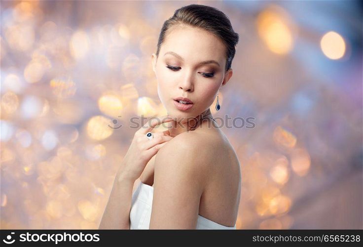 beauty, jewelry, people and luxury concept - beautiful asian woman or bride with earring and finger ring over holidays lights background. beautiful woman with earring and finger ring