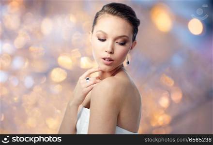 beauty, jewelry, people and luxury concept - beautiful asian woman or bride with earring and finger ring over holidays lights background. beautiful woman with earring and finger ring