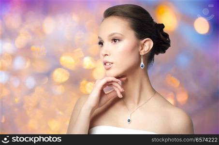 beauty, jewelry, people and luxury concept - beautiful asian woman or bride with earring and pendant over holidays lights background. beautiful asian woman with earring and pendant