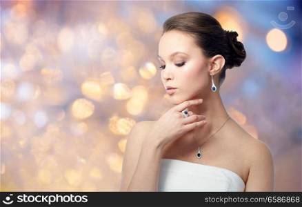beauty, jewelry, people and luxury concept - beautiful asian woman or bride with earring and pendant over holidays lights background. beautiful asian woman with earring and pendant