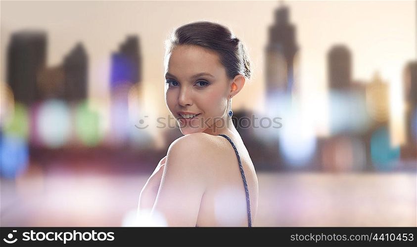 beauty, jewelry, people and luxury concept - beautiful young asian woman with earring over city silhouette and lights background