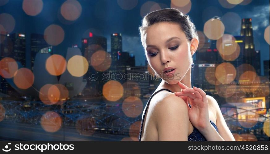 beauty, jewelry, people and luxury concept - beautiful young asian woman with earring over singapore city night lights background