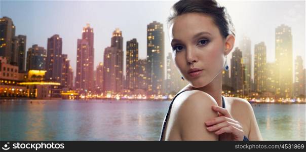 beauty, jewelry, people and luxury concept - beautiful young asian woman with earring over dubai city night lights background