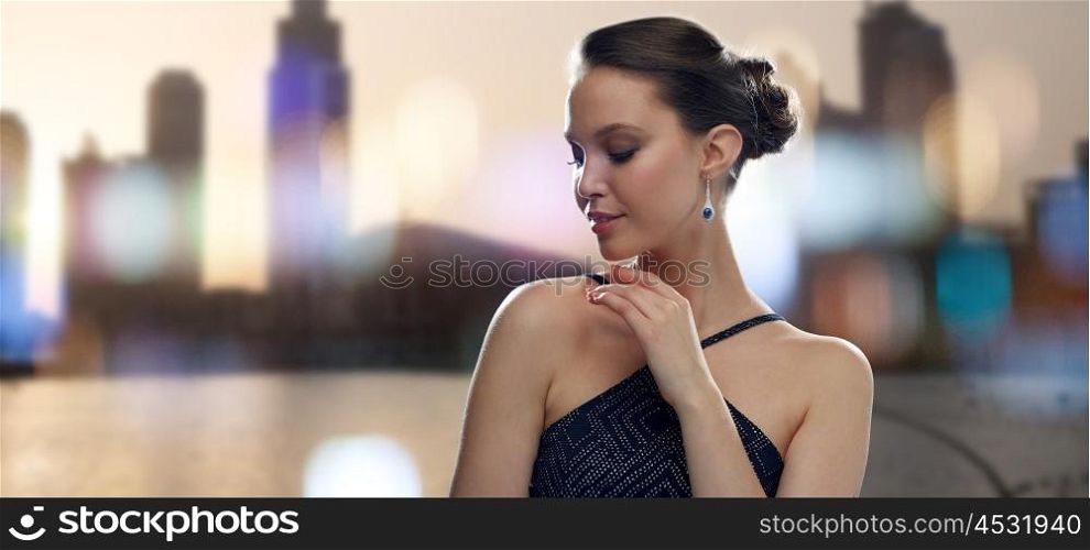 beauty, jewelry, people and luxury concept - beautiful young asian woman with earring over city silhouette and lights background