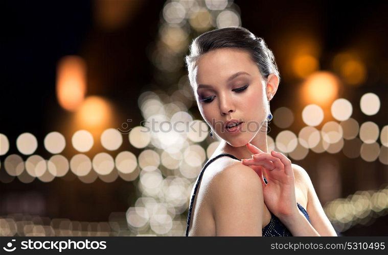 beauty, jewelry, people and luxury concept - beautiful young asian woman with earring over christmas tree lights background. beautiful asian woman with earrings at christmas