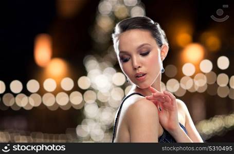 beauty, jewelry, people and luxury concept - beautiful young asian woman with earring over christmas tree lights background. beautiful asian woman with earrings at christmas