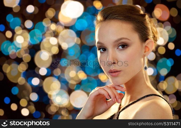 beauty, jewelry, people and luxury concept - beautiful young asian woman with earring over holidays lights background. beautiful young asian woman with earring