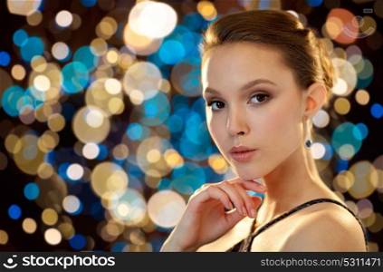 beauty, jewelry, people and luxury concept - beautiful young asian woman with earring over holidays lights background. beautiful young asian woman with earring