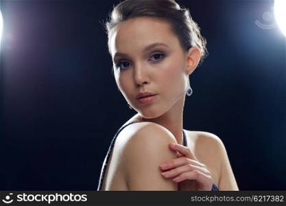 beauty, jewelry, people and luxury concept - beautiful young asian woman with earring over black background and spotlights
