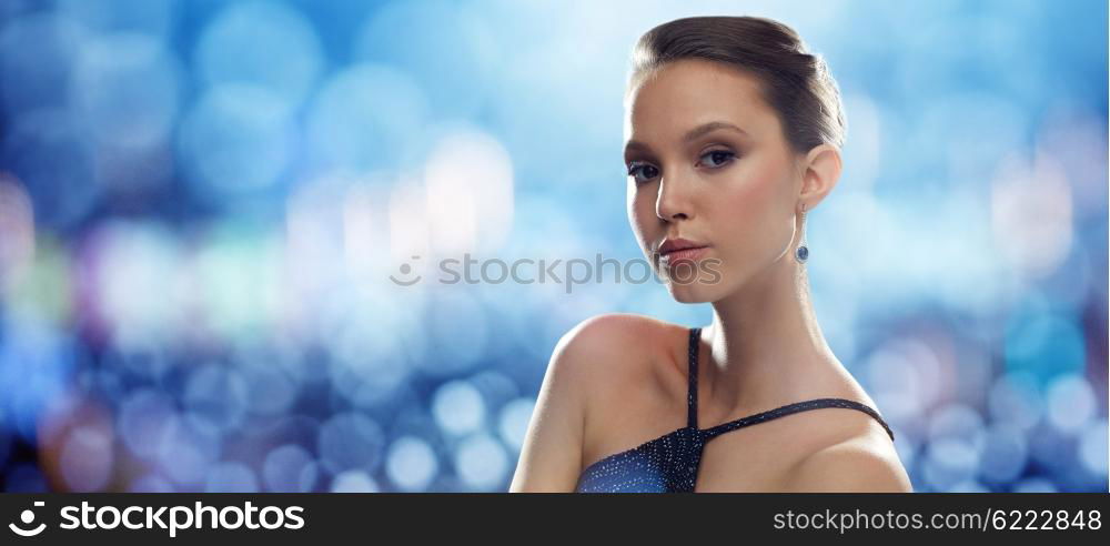 beauty, jewelry, people and luxury concept - beautiful young asian woman with earring over blue lights background