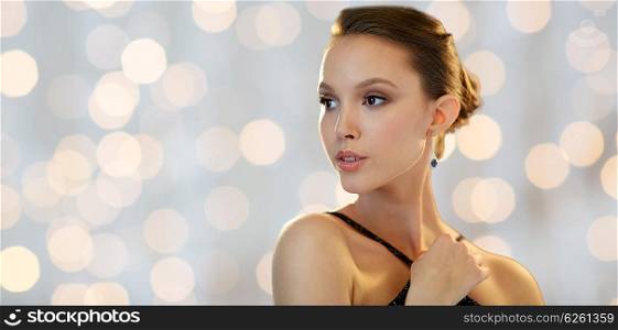 beauty, jewelry, people and luxury concept - beautiful young asian woman with earring over holidays lights background