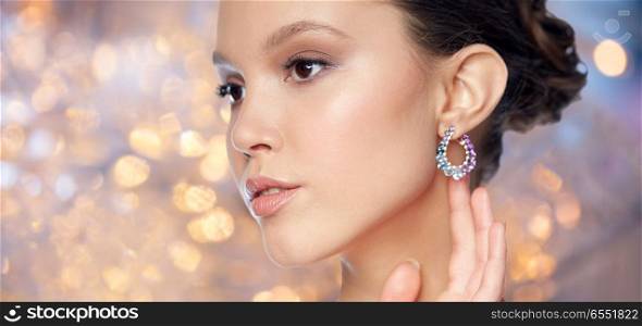 beauty, jewelry, people and luxury concept - close up of beautiful asian woman face with earring over holidays lights background. close up of beautiful woman face with earring. close up of beautiful woman face with earring
