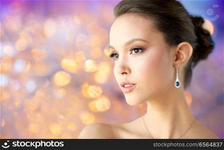 beauty, jewelry, people and luxury concept - close up of beautiful asian woman or bride with earring over holidays lights background. close up of beautiful woman face with earring