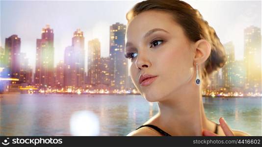 beauty, jewelry, people and luxury concept - face of beautiful young asian woman with earring over dubai city night lights background