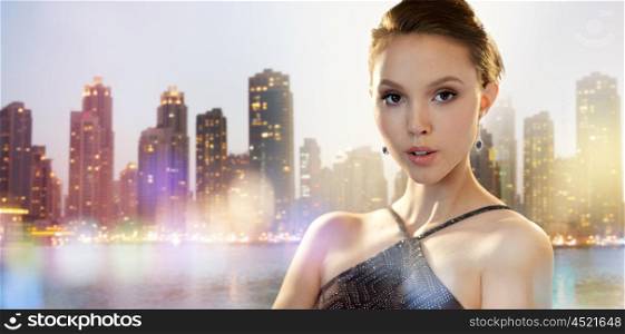 beauty, jewelry, people and luxury concept - face of beautiful young asian woman with earring over dubai city night lights background