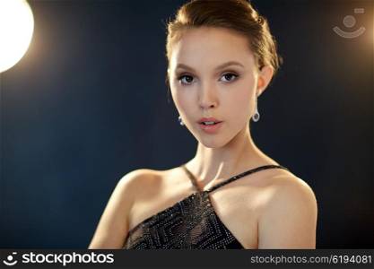 beauty, jewelry, people and luxury concept - face of beautiful young asian woman with earring over black background and spotlights