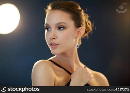 beauty, jewelry, people and luxury concept - face of beautiful young asian woman with earring over black background and spotlights