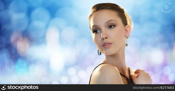 beauty, jewelry, people and luxury concept - face of beautiful young asian woman with earring over blue lights background