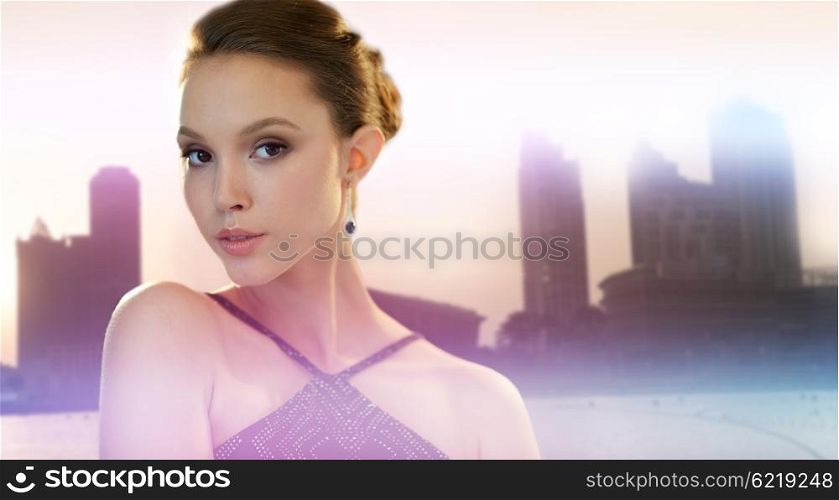 beauty, jewelry, people and luxury concept - face of beautiful young asian woman with earring over city silhouette and lights background