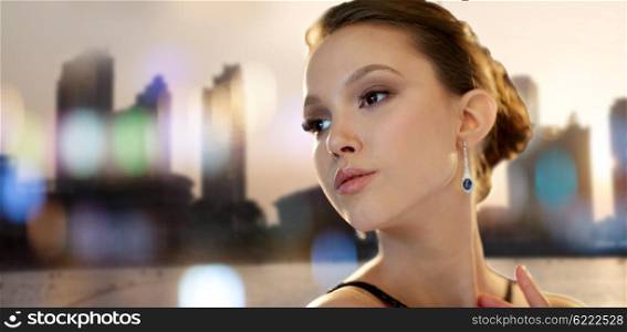 beauty, jewelry, people and luxury concept - face of beautiful young asian woman with earring over city silhouette and lights background