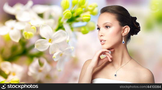 beauty, jewelry, wedding accessories, people and luxury concept - beautiful asian woman or bride with earring and pendant over natural spring lilac blossom background