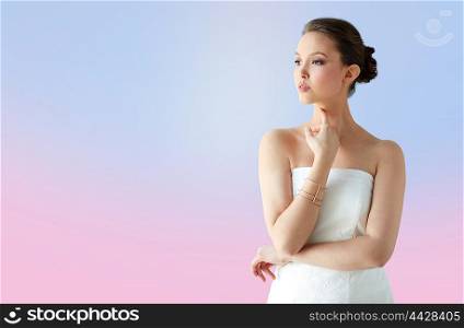 beauty, jewelry, wedding accessories, people and luxury concept - beautiful asian woman in white dress or bride with golden bracelet over rose quartz and serenity gradient background