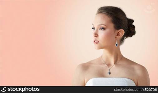 beauty, jewelry, wedding accessories, people and luxury concept - beautiful asian woman or bride with earring and pendant over beige background