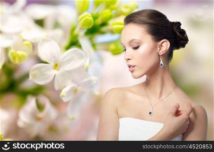 beauty, jewelry, wedding accessories, people and luxury concept - beautiful asian woman or bride with earring and pendant over natural spring lilac blossom background