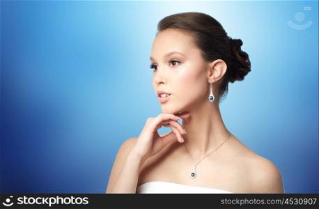beauty, jewelry, wedding accessories, people and luxury concept - beautiful asian woman or bride with earring and pendant over blue background