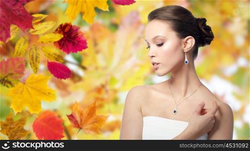 beauty, jewelry, wedding accessories, people and luxury concept - beautiful asian woman or bride with earring and pendant over autumn leaves background